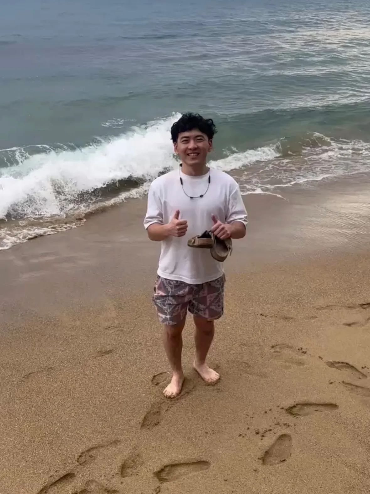 Benji giving two thumbs up, barefoot on a beach in Puerto Rico on a trip with friends